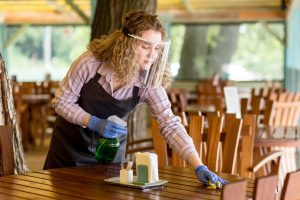 woman with face protection cleaning tables 300x200
